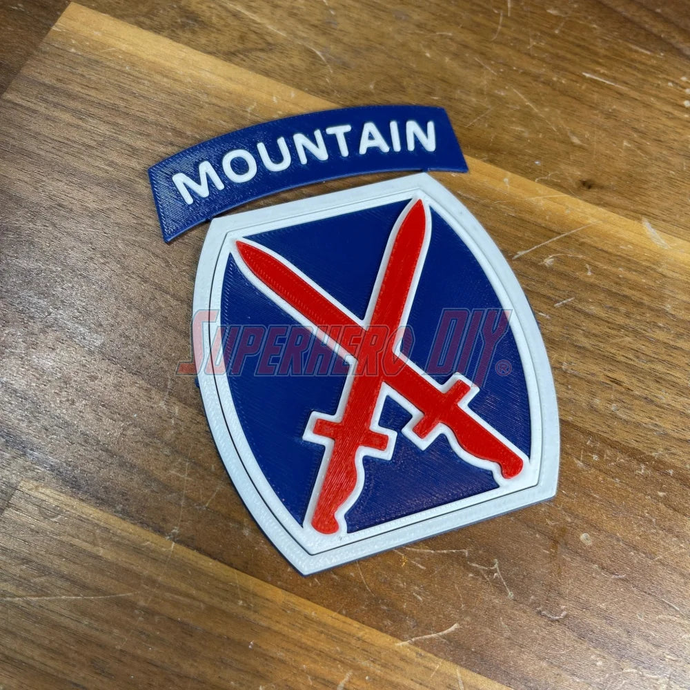3D-printed 10th Mountain Division insignia with red, white, and blue design on wooden surface.