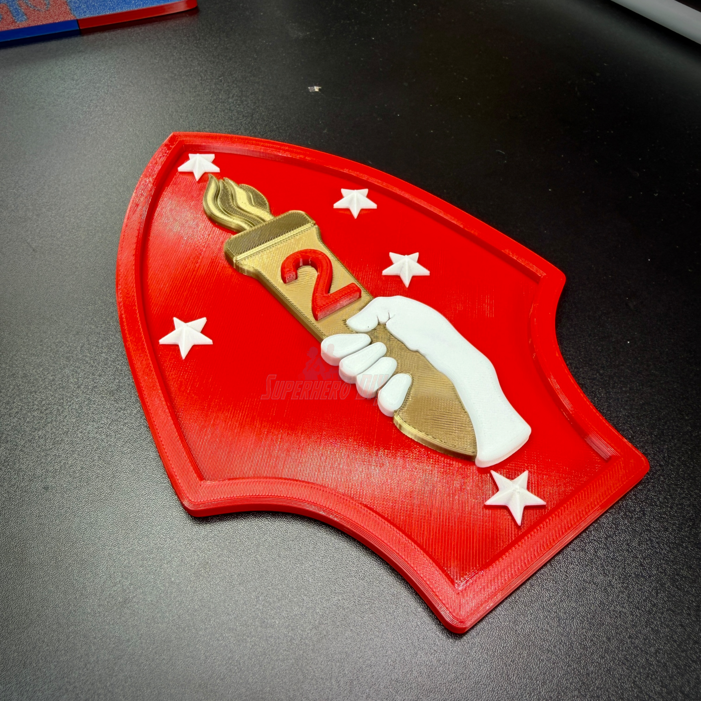 2nd Marine Division display insignia featuring a red shield with a gold torch, stars, and a hand holding a torch.