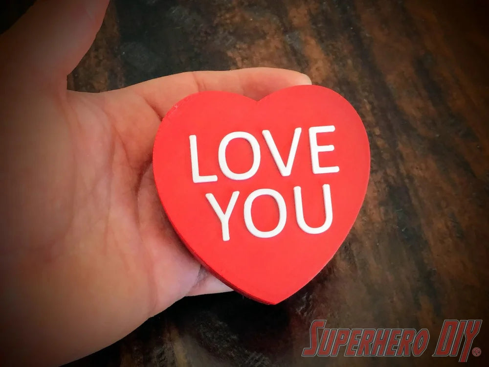 3D-PRINTABLE STL FILE | Candy Heart Gift Box | DIGITAL FILE ONLY - Red heart-shaped candy box with white "LOVE YOU" text held in hand on dark wooden surface. - SuperheroDIY