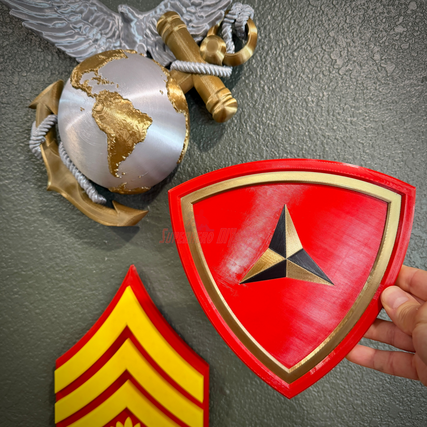 3rd Marine Division insignia held by a hand, featuring a red shield with gold accents and three-pointed caltrap.