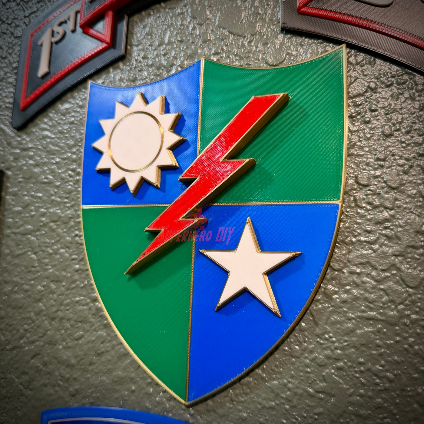 A close-up of a shield-shaped emblem mounted on a textured gray wall. The shield is divided into four quadrants: blue in the upper left, green in the upper right, blue in the lower left, and green in the lower right, with a red lightning bolt running diagonally across the center.