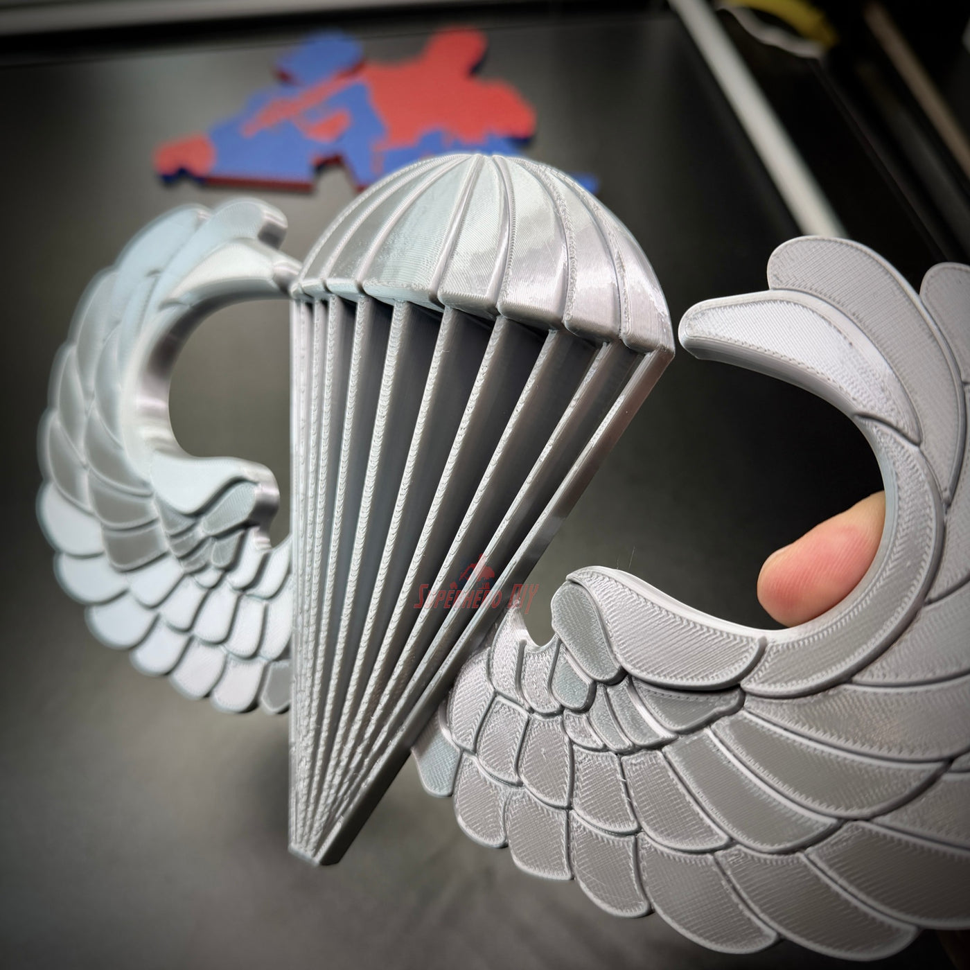 Close-up of a silver airborne jump wings badge featuring a parachute and wings design.