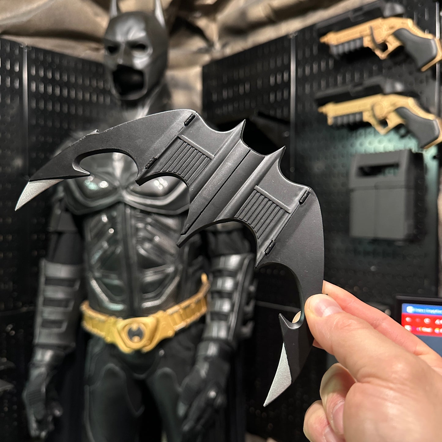 NECA BATMAN 1989 Folding Magnetic Batarang (LOOSE) held in front of a Batman display in a Batcave setting.