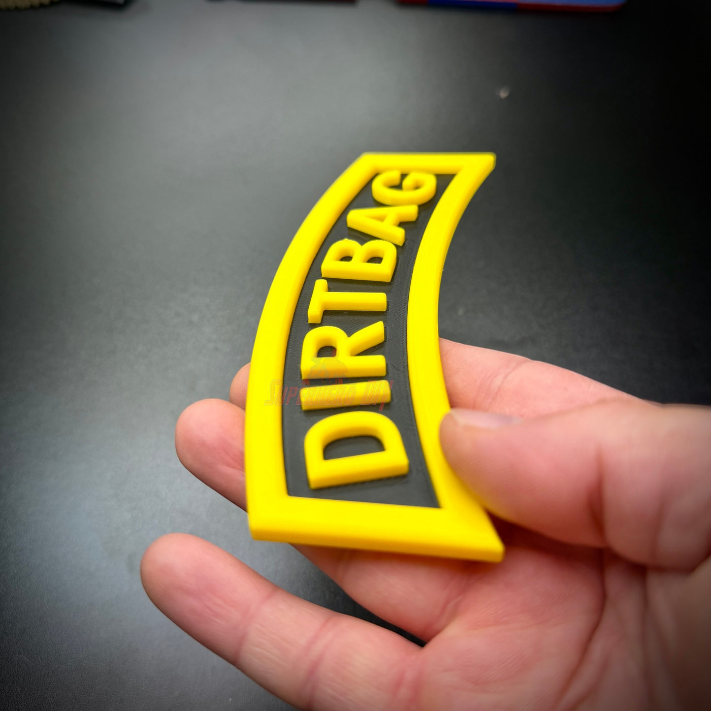 Close-up of DIRTBAG tab, a yellow and black gag gift rocker for soldiers.