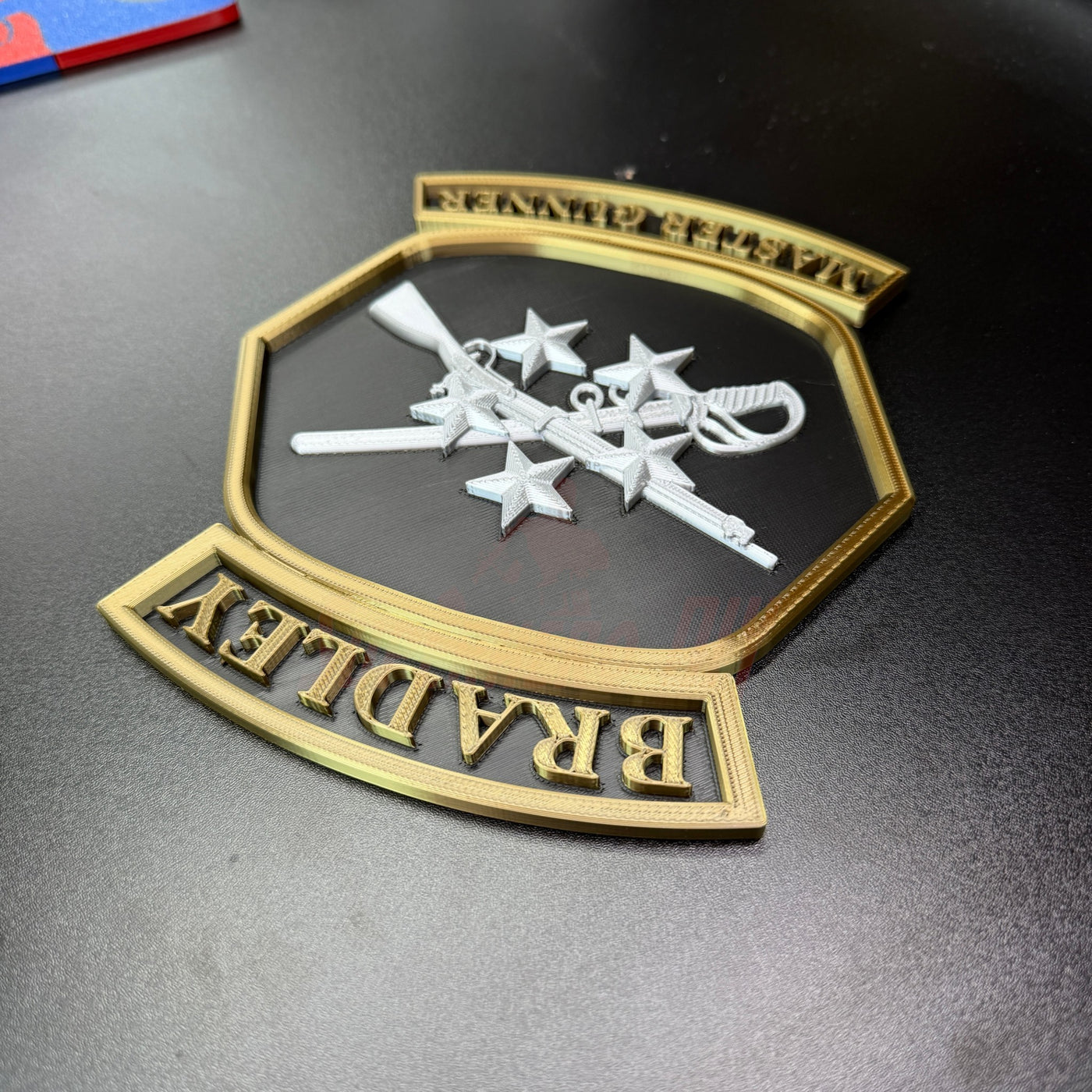 3D representation of the Bradley Master Gunner Badge display with crossed weapons and stars in bold relief.