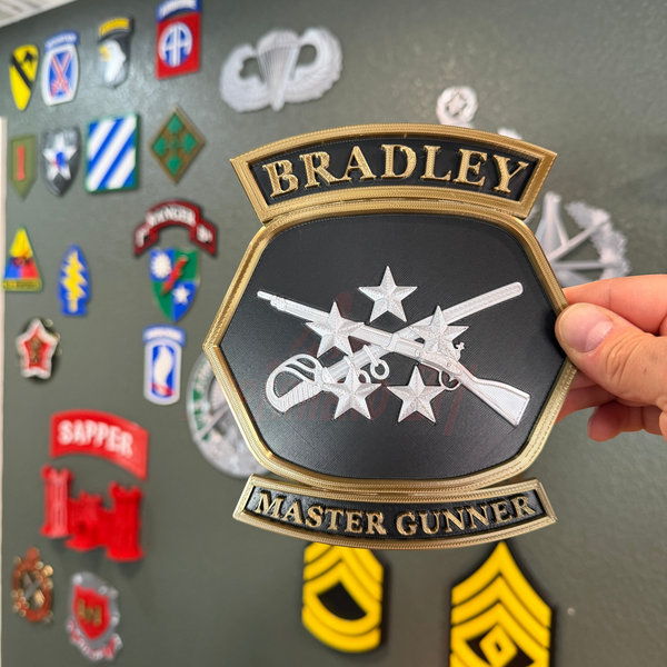 Bradley Master Gunner Badge display held in hand with crossed weapons and stars, showcasing intricate design.