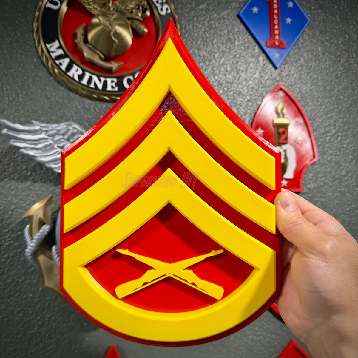 USMC Sergeant (E-5) insignia held up in front of a wall of Marine Corps emblem and unit insignia displays