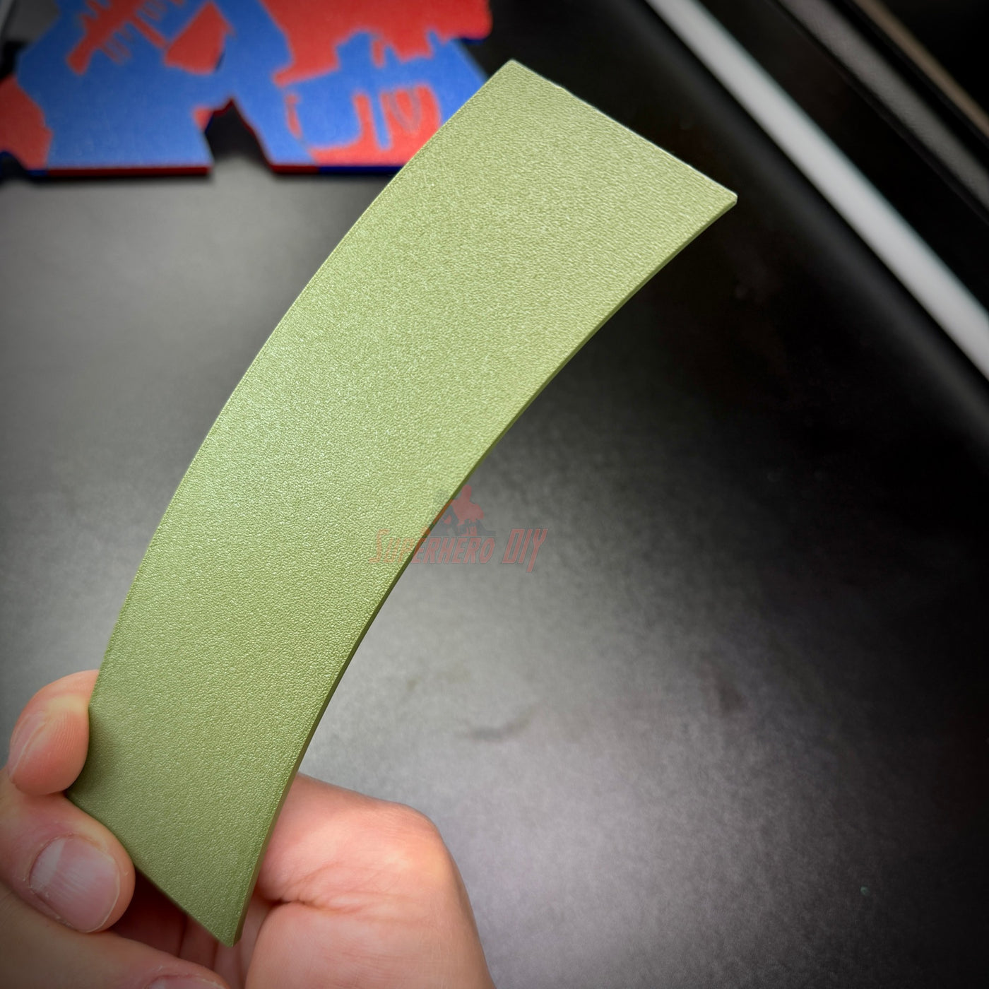 Hand holding a curved army green wall display piece resembling a jungle tab.