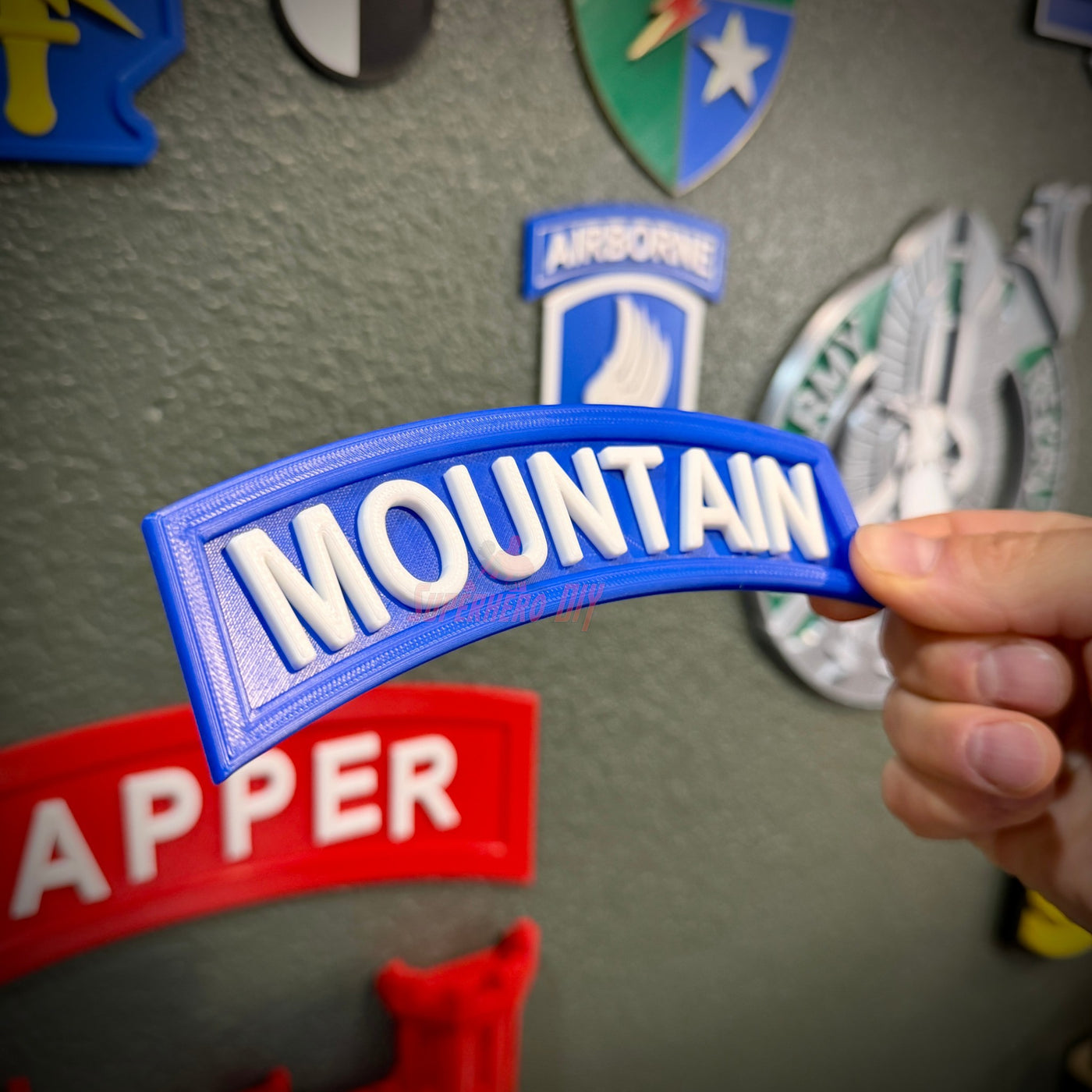 3D mountain tab wall display with raised white lettering against a blue background, held by a hand.