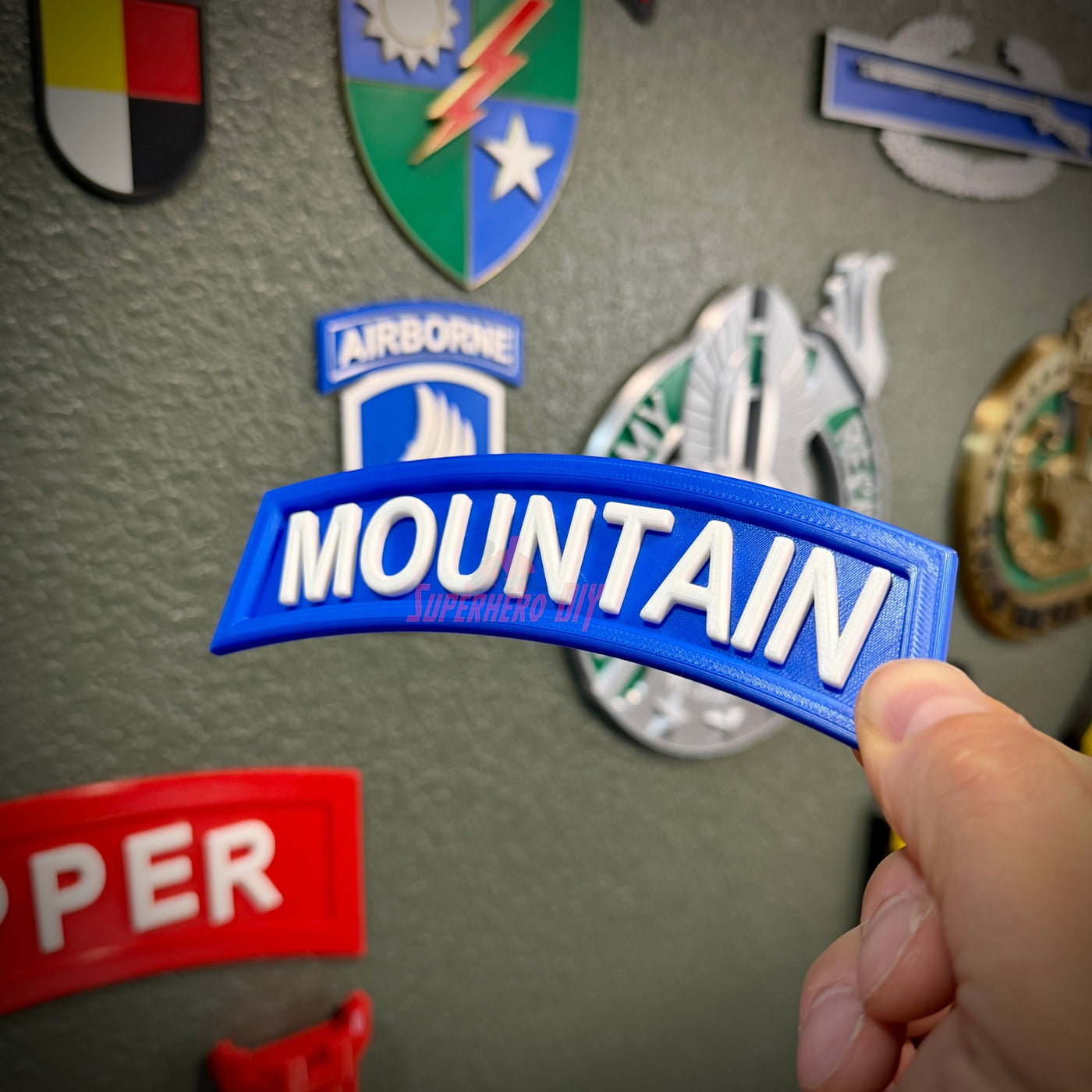 3D mountain tab wall display in hand against a backdrop of various military patches