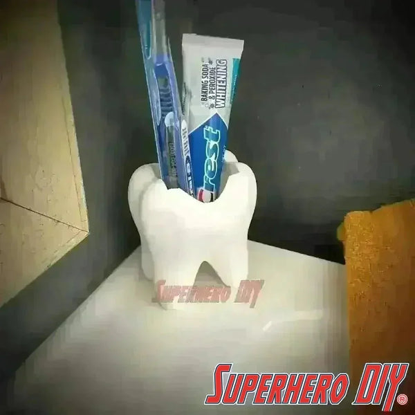 Tooth shaped bathroom organizer holding toothbrush and toothpaste on a sink. Functional design and unique decor for your home.