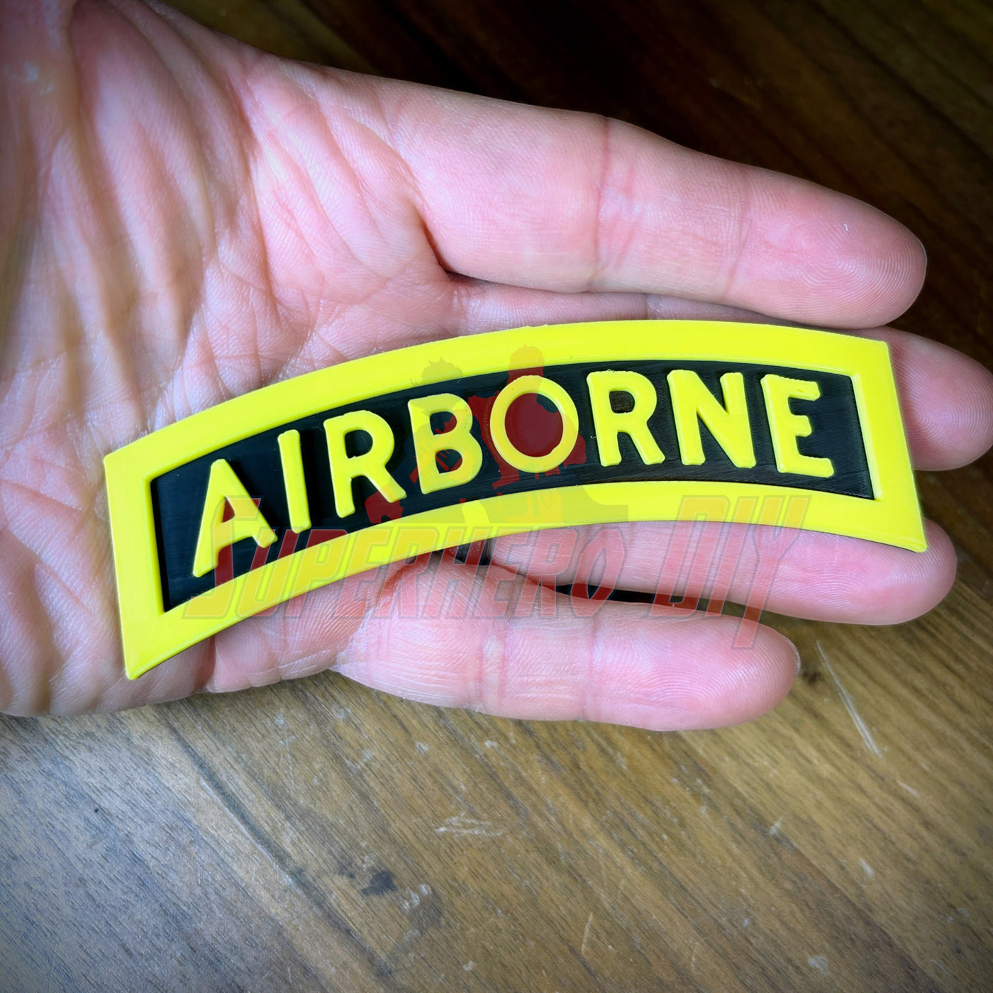 3D airborne tab in hand displaying bold yellow letters on a solid black background, perfect for military shadow boxes.