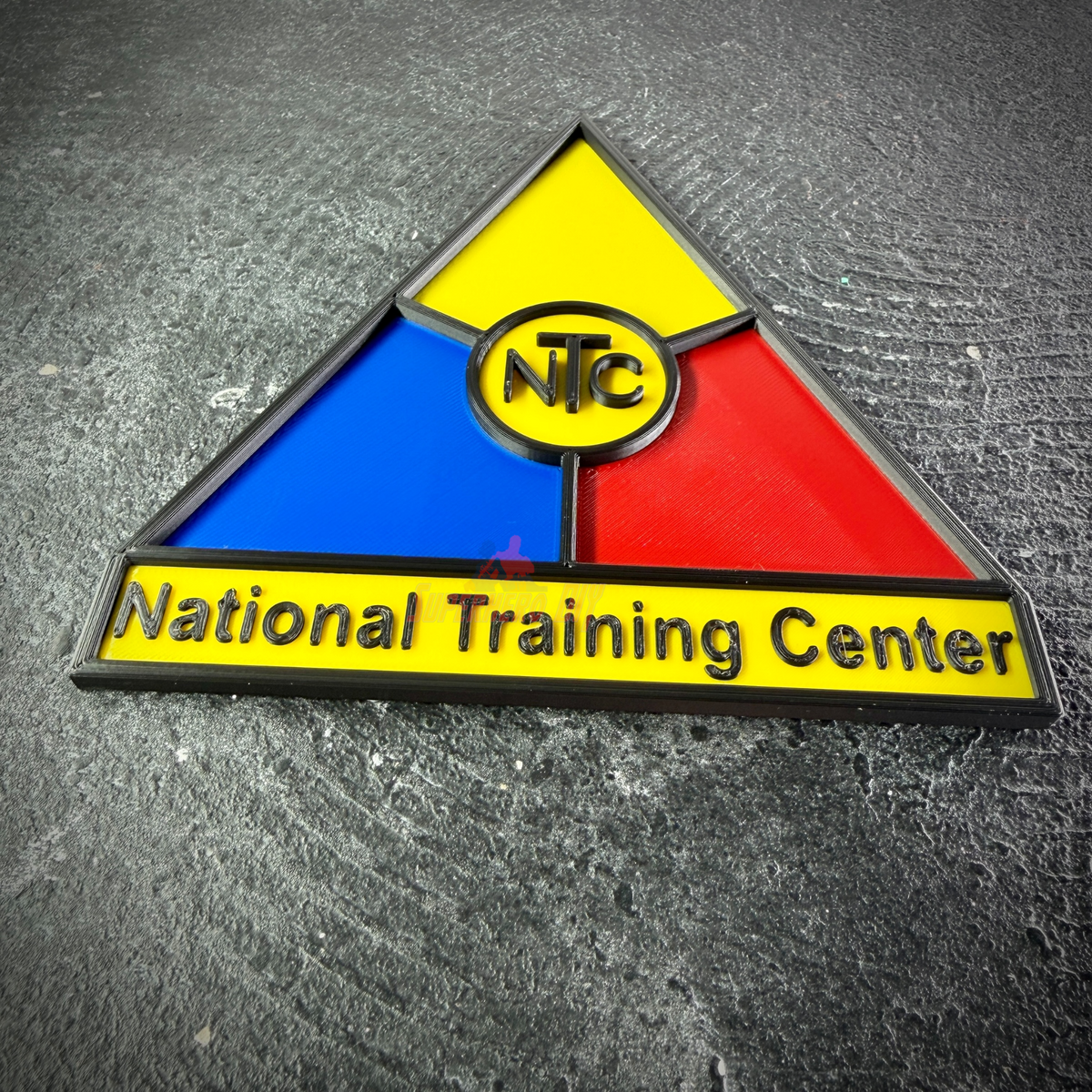 Low side angle of the NTC display insignia showing raised black borders and lettering on the yellow banner