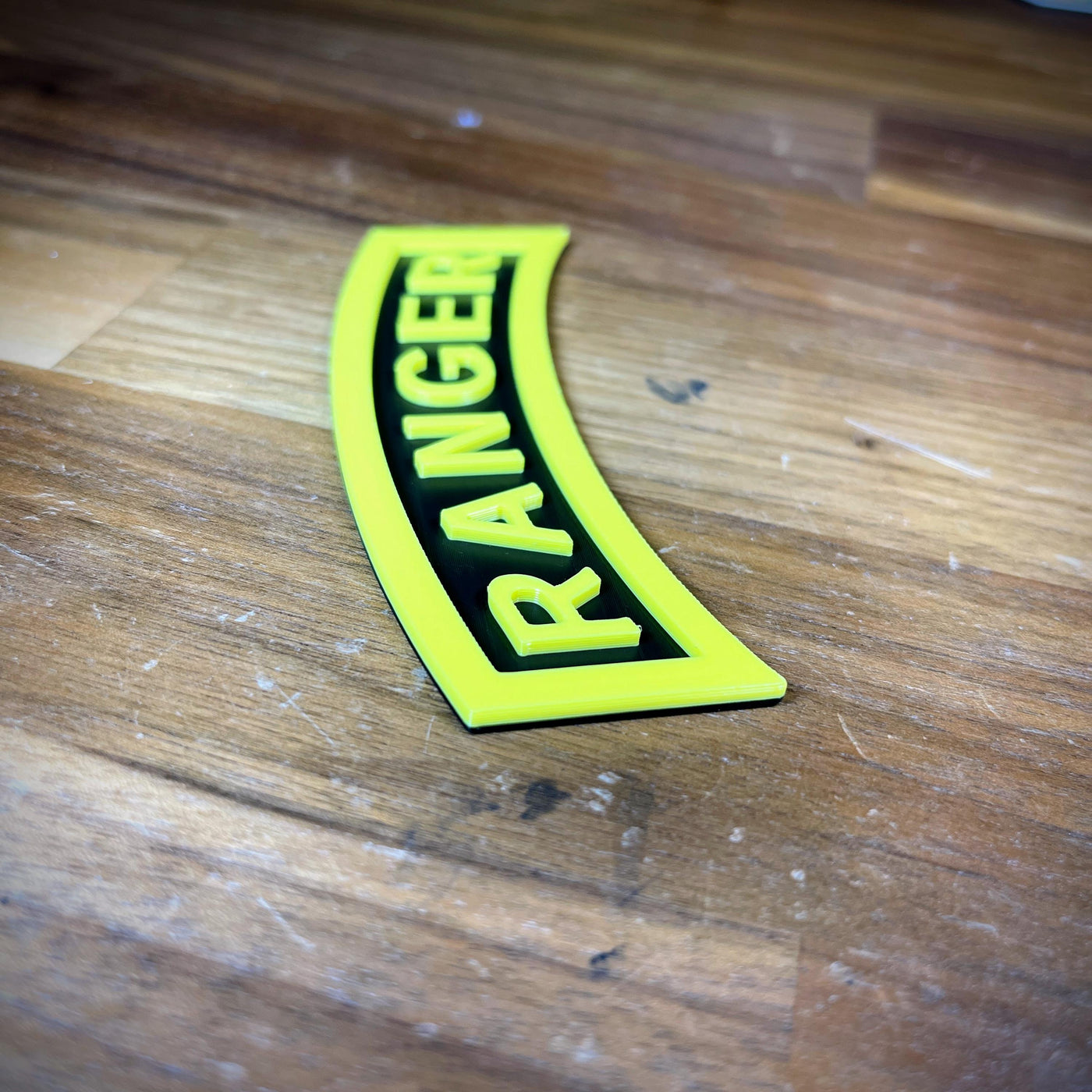 3D Army Ranger Tab in yellow and black displayed on a wooden surface, showcasing intricate design details.