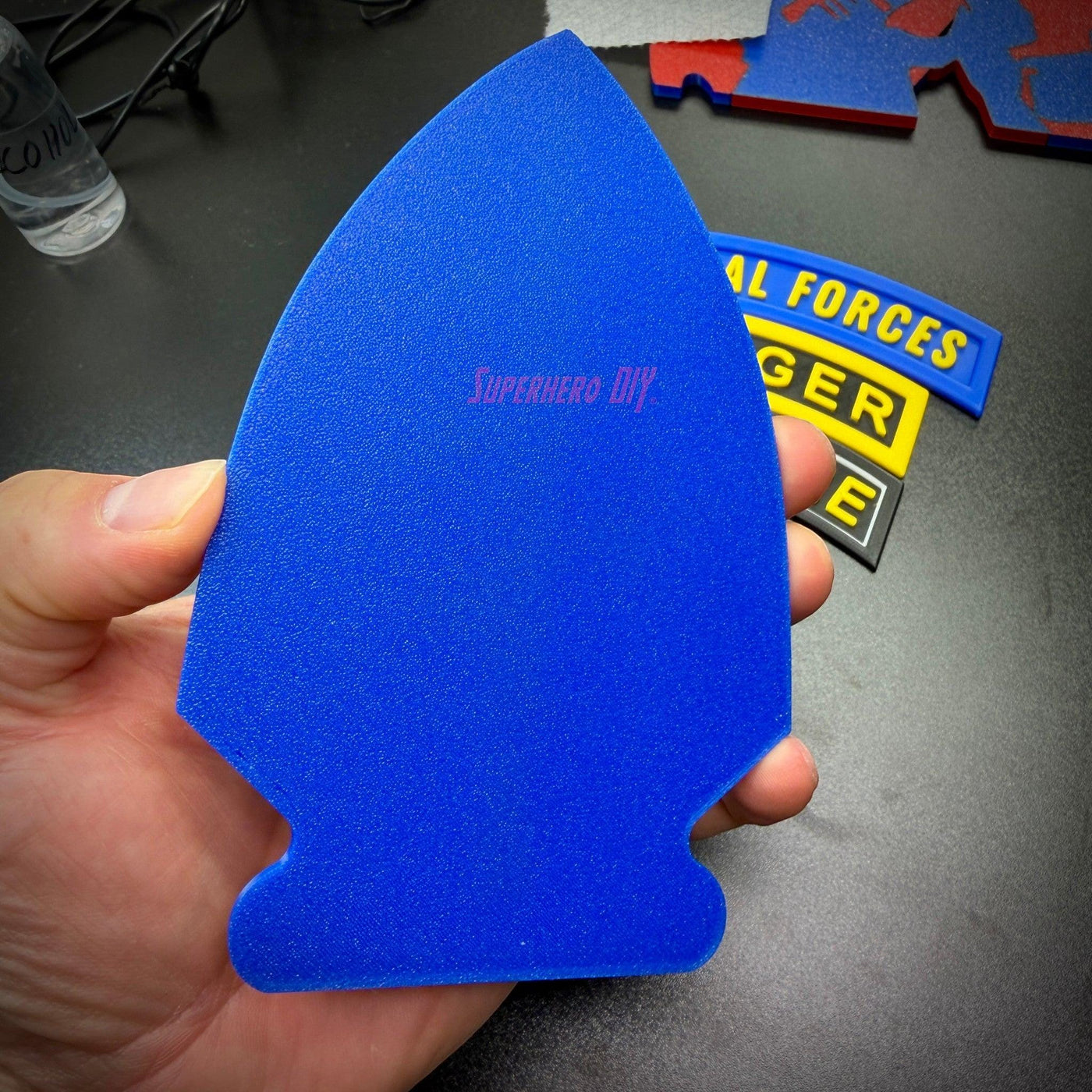 Special Forces display insignia blue arrowhead piece held by a hand, part of insignia set for wall display or shadow box.