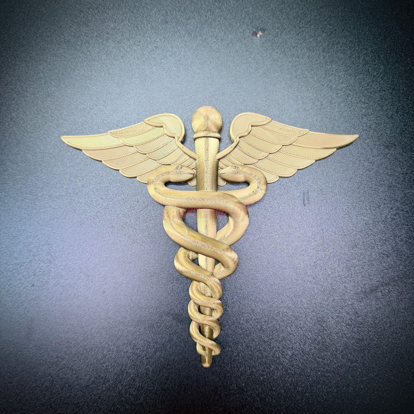 Gold army medical corps caduceus wall display with wings and serpents on dark background.