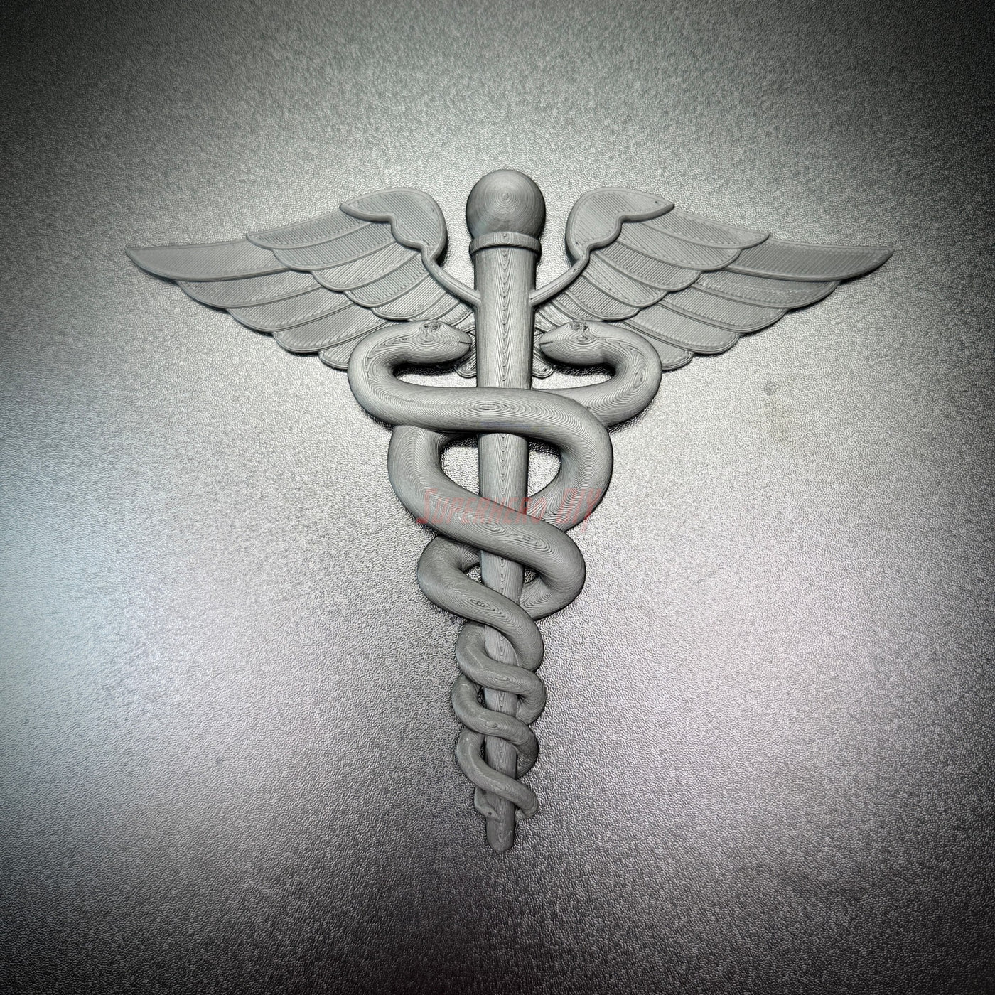 Army medical corps caduceus wall display in gray, featuring a staff with twin serpents and wings.