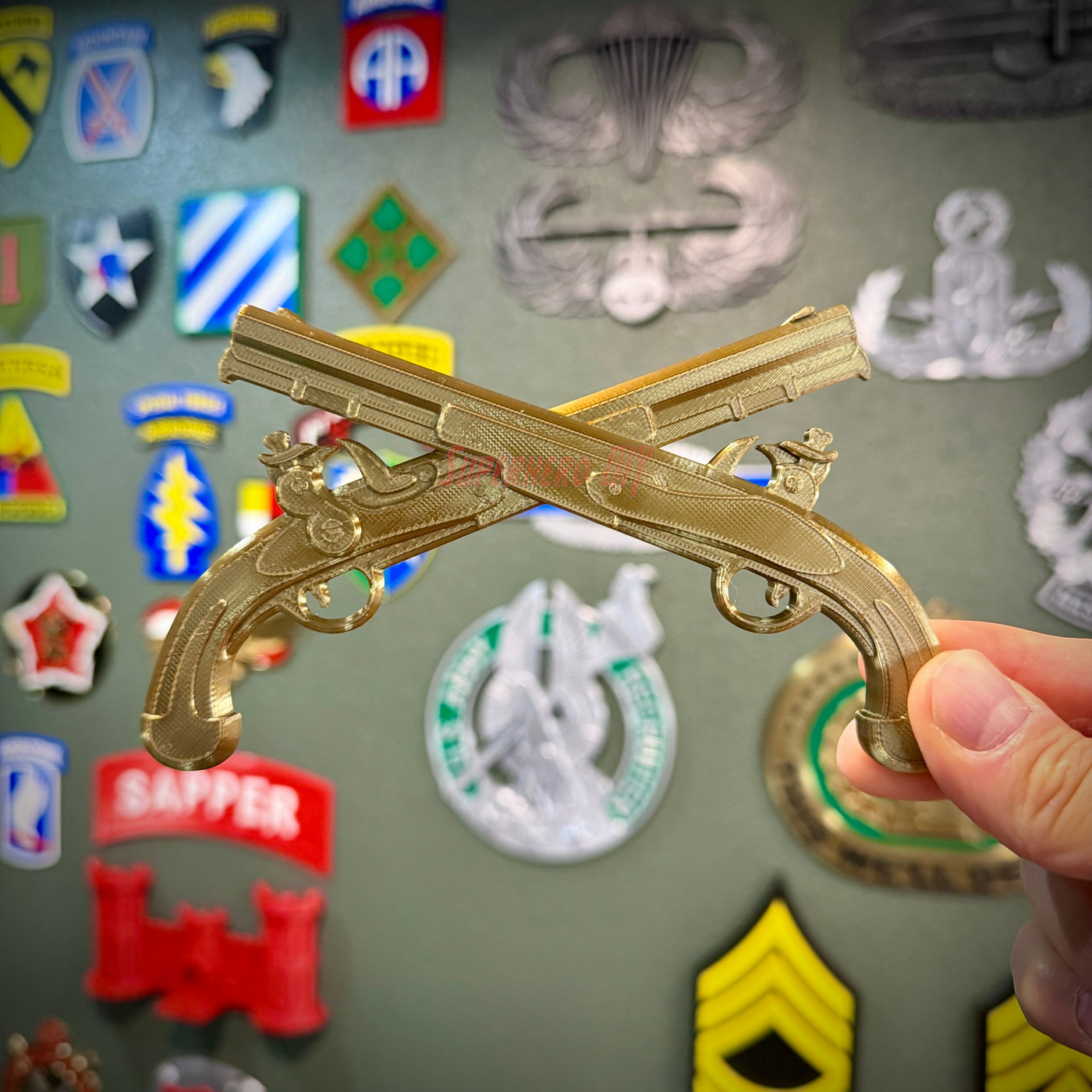 Army military police insignia, crossed pistols display in gold held against a background of military patches.