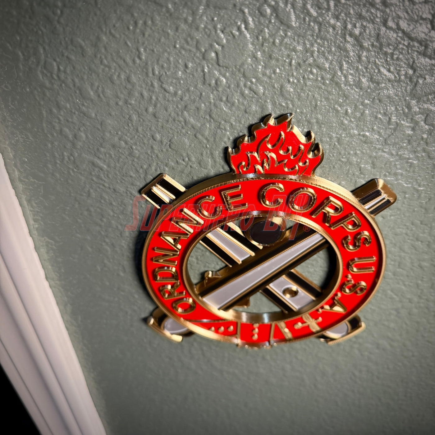 Ordnance Regimental Crest displayed on a wall, symbolizing the Ordnance Corps with red and gold colors.