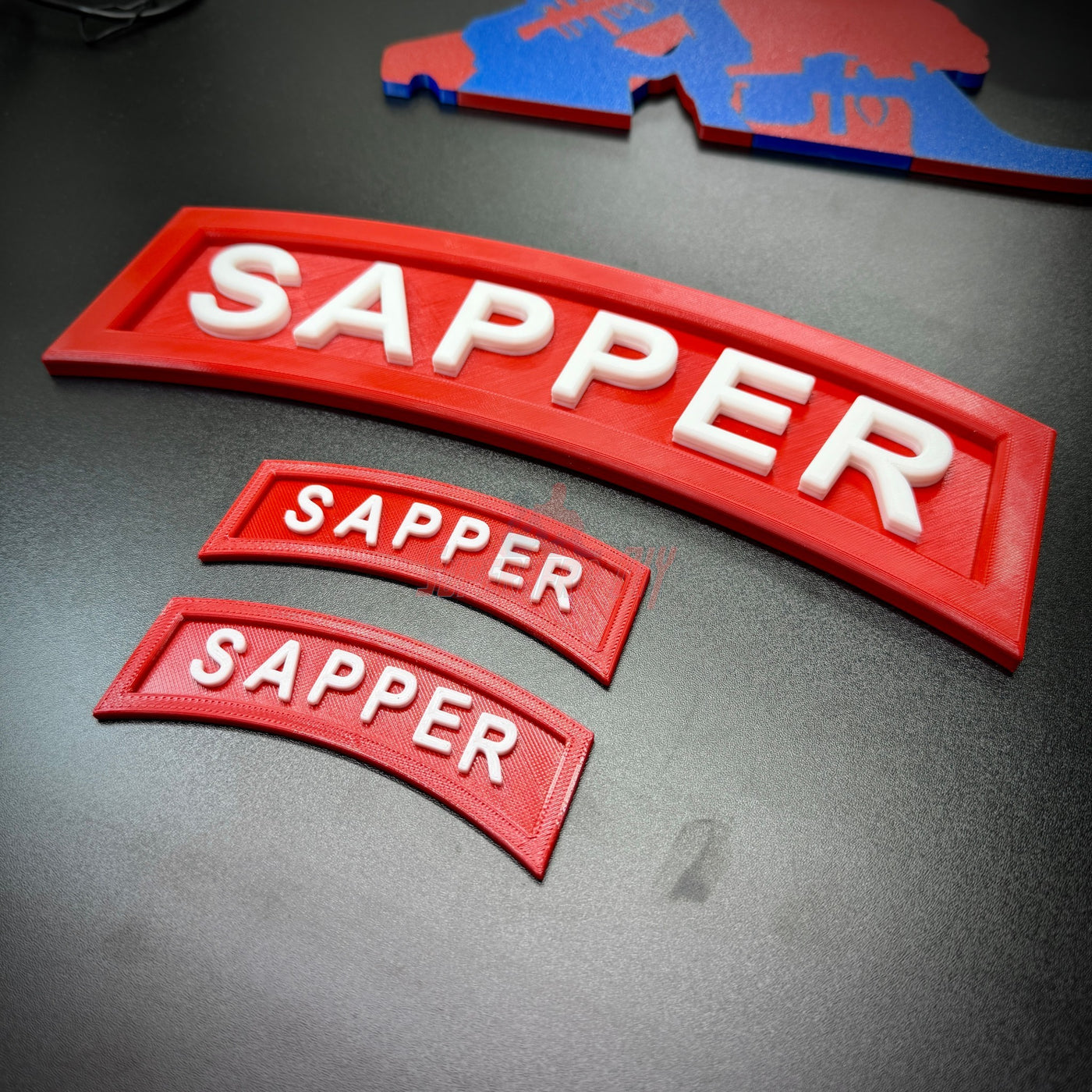 3D sapper tab in red with white letters displayed in three sizes on a black surface.