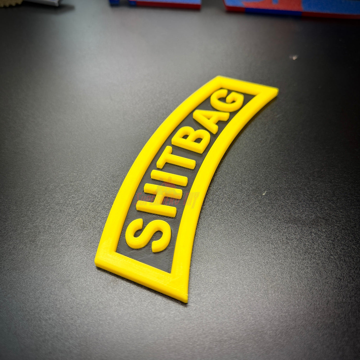 Close-up of SHITBAG tab in black and yellow, perfect gag gift for soldiers and battle buddies.