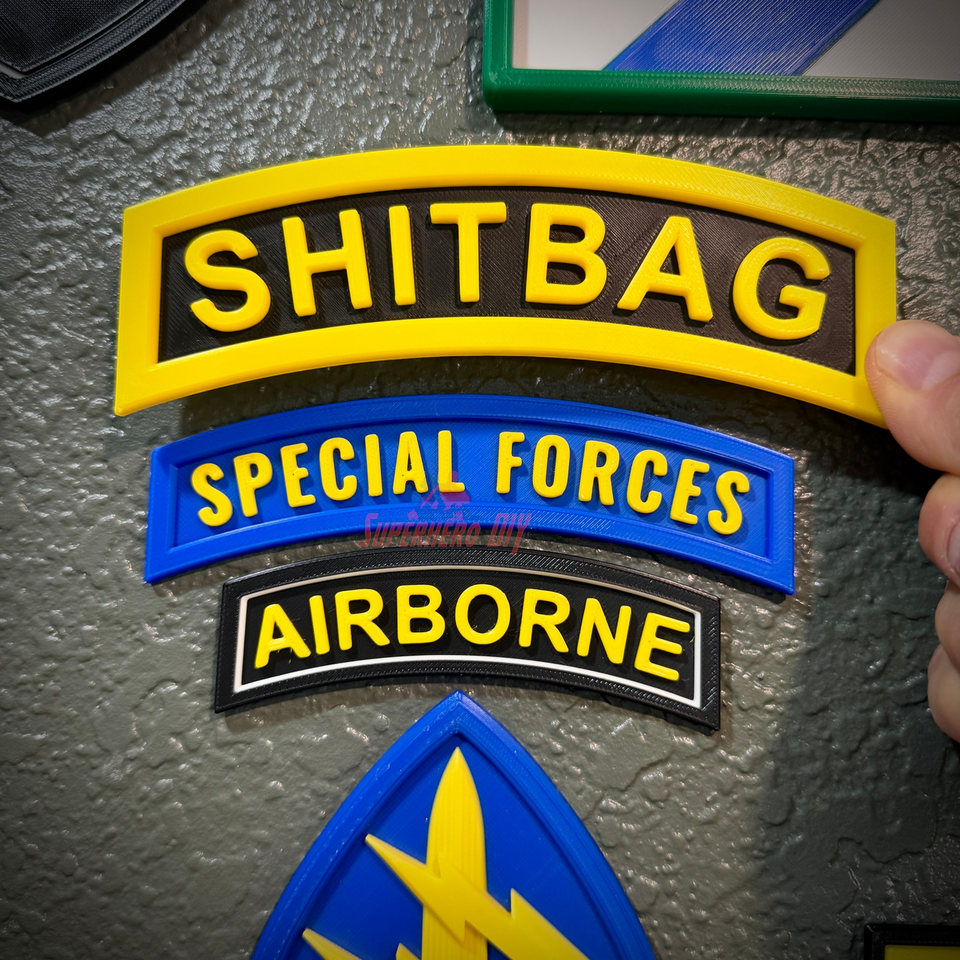 Image of SHITBAG tab along with Special Forces and Airborne patches on a wall display.