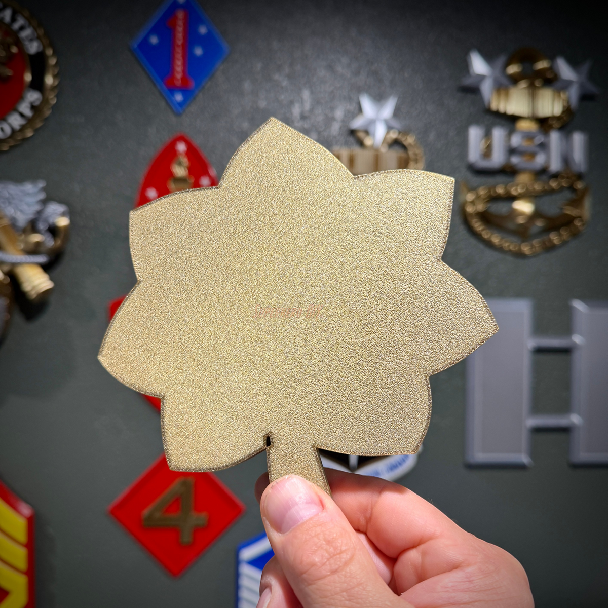 O-4 Major Navy lieutenant commander rank insignia in gold silk finish held against a backdrop of military insignias.