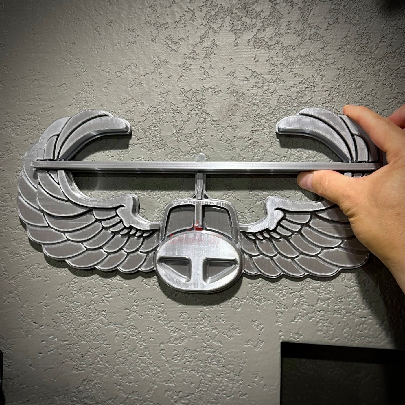 Air Assault Badge display showing shiny silver finish and detailed wings being mounted on a wall.