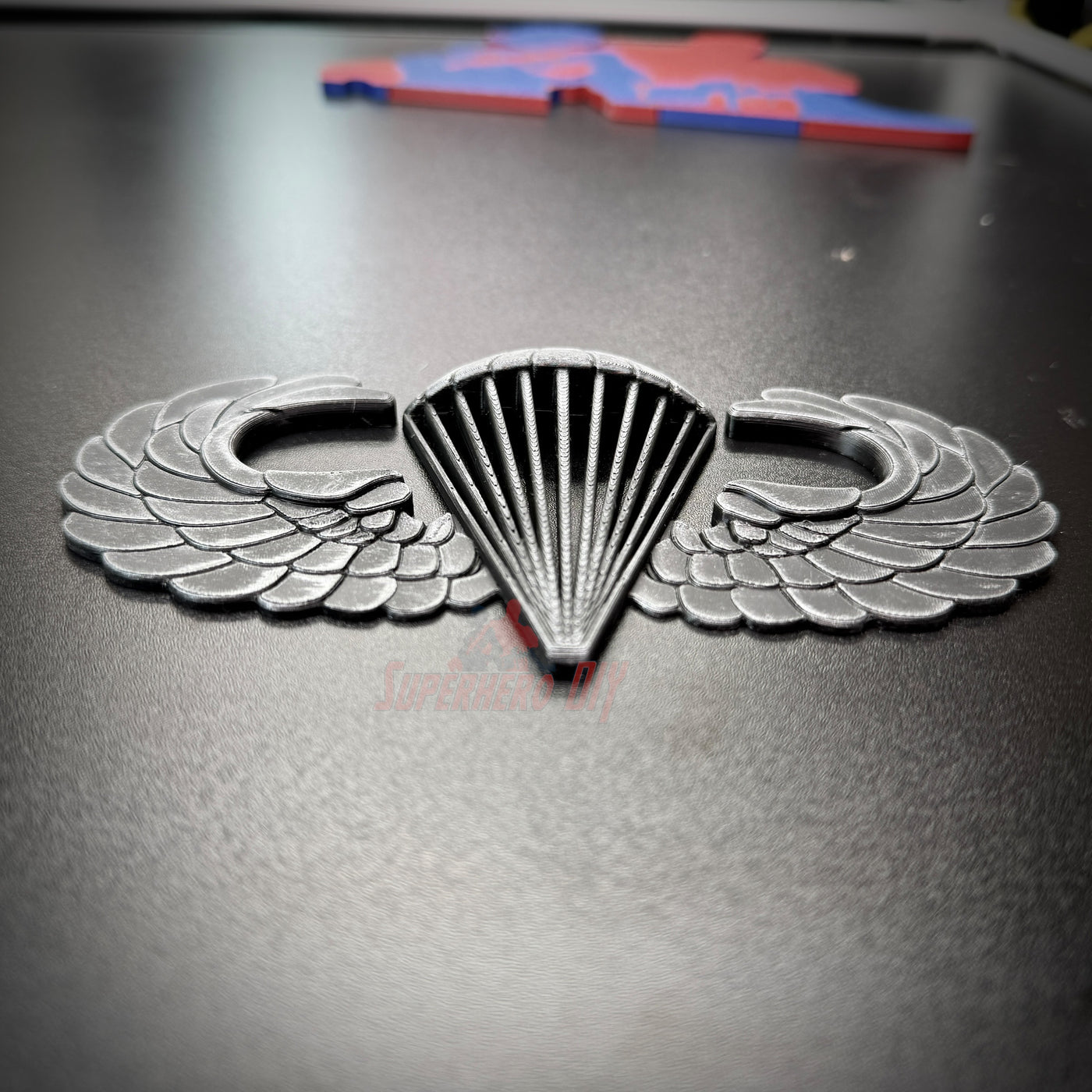 Subdued airborne jump wings badge with detailed wing design on a black background.
