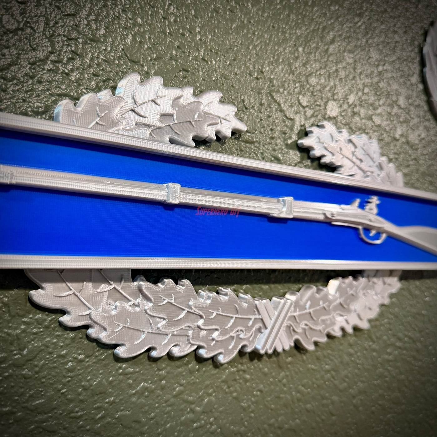 Combat Infantryman Badge replica display with musket on infantry-blue bar and oak wreath.