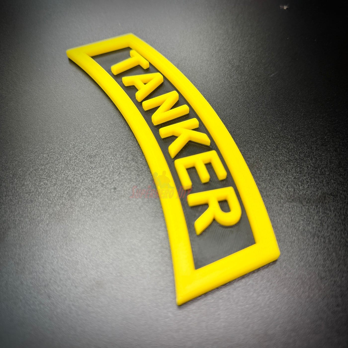 3D tanker tab in bright yellow with raised lettering, showcasing the word 'TANKER' prominently.