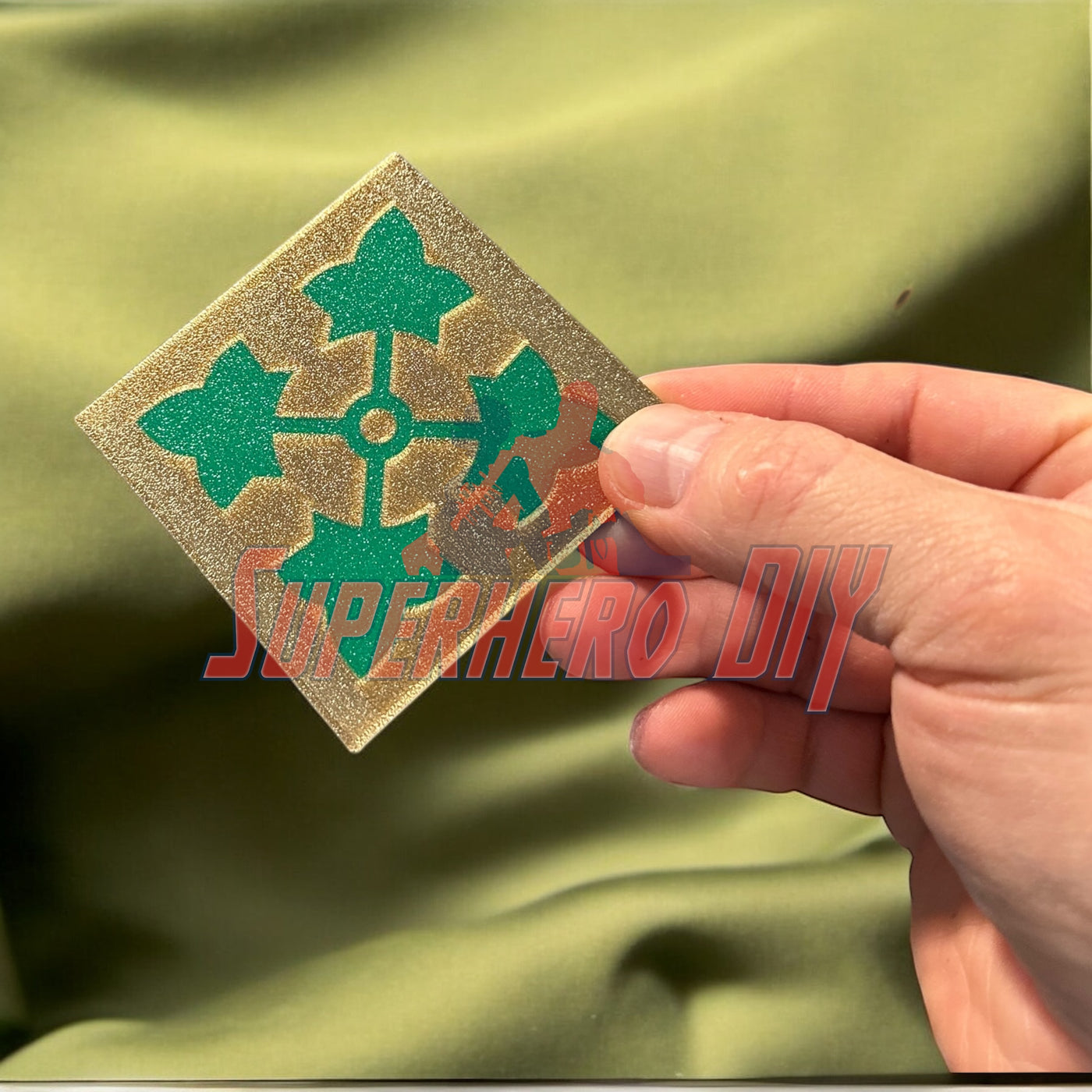 Hand holding 4th Infantry Division display insignia with iconic ivy leaf patch on green background