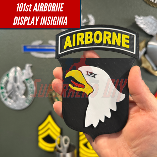 Hand holding 101st Airborne Division display insignia with eagle design and various ranks in background