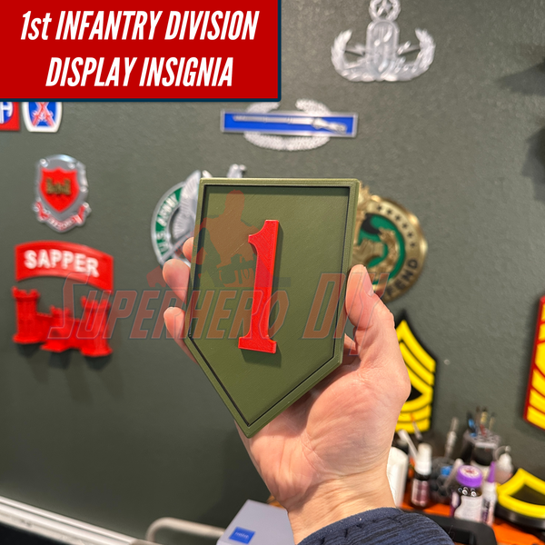 Person holding the 1st Infantry Division display insignia, also known as the Big Red One patch, with other military insignias in the background.