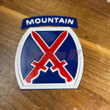 3D-printed 10th Mountain Division insignia with blue, red, and white design on wooden surface