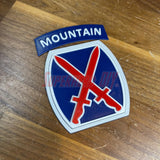 3D-printed 10th Mountain Division insignia with red, white, and blue design on wooden surface.