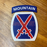 3D-printed 10th Mountain Division insignia with blue, red, and white design on a wooden background.