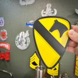 Person holding a 1st Cavalry Division Display Insignia in front of a wall with military decor.