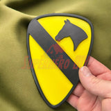 1st Cavalry Division Display Insignia being held against fabric, showcasing its distinct design with a yellow background and black emblem.