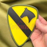 1st Cavalry Division Display Insignia in hand, featuring a black horse head on a yellow background with a diagonal black stripe.