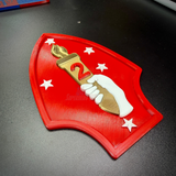 2nd Marine Division display insignia featuring a red shield with a gold torch, stars, and a hand holding a torch.