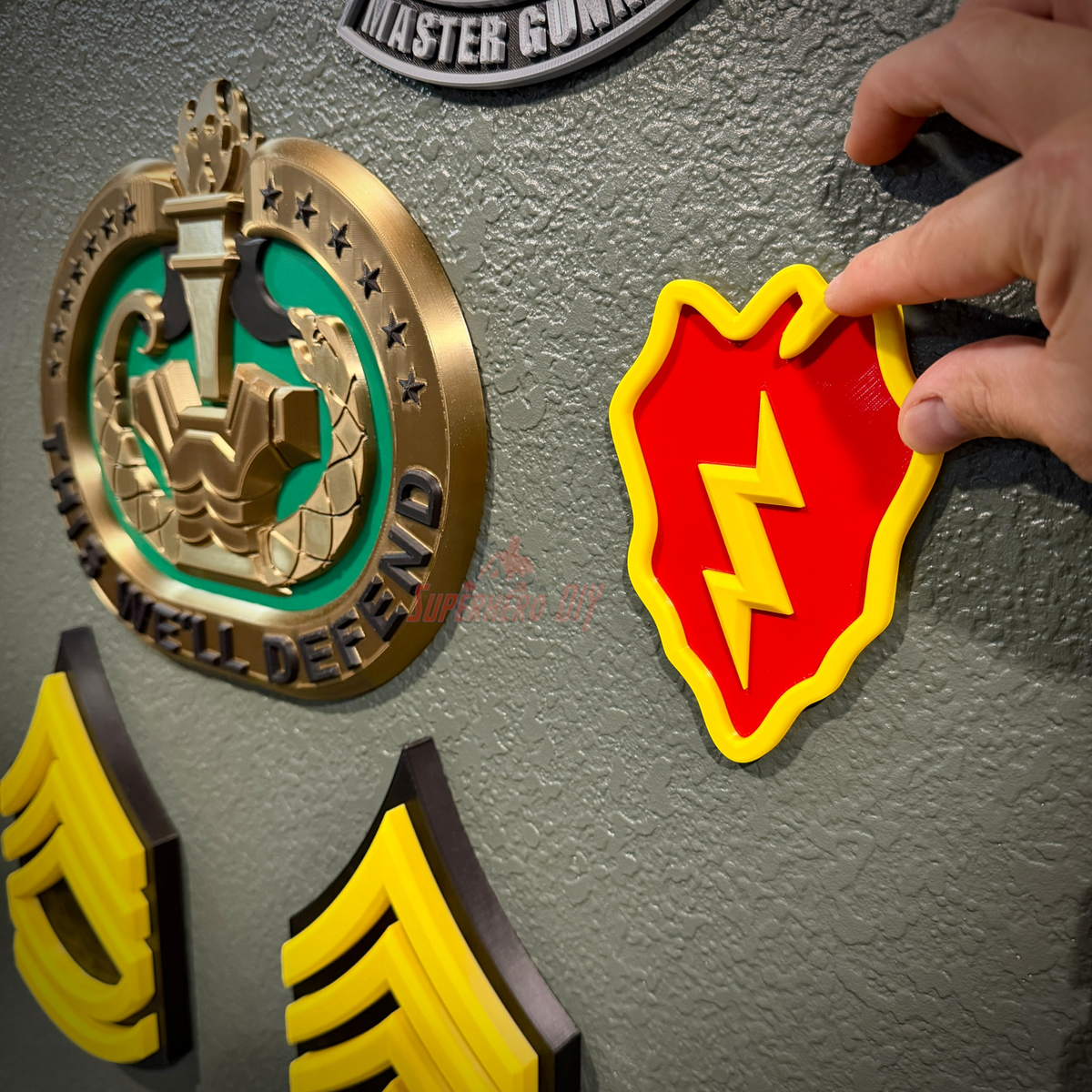 25th Infantry Division insignia being pressed onto a gray wall beside other military insignia and rank chevron displays
