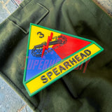 3rd Armored Division display insignia with Spearhead emblem, colorful design on green fabric background.