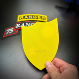 75th Ranger Regiment display insignia in yellow shape held by hand on a black surface with Ranger patches.