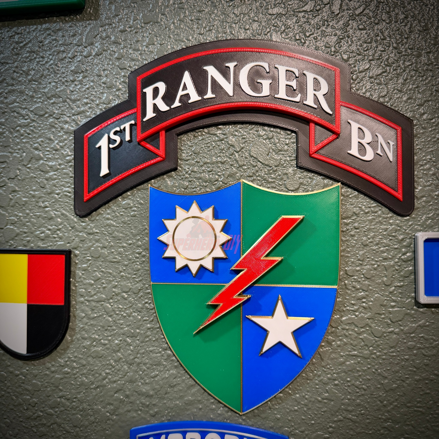 A close-up of a decorative wall sign featuring the '1st Ranger BN' insignia, with a multicolor shield and a textured gray wall background.