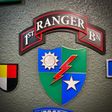 A close-up of a decorative wall sign featuring the '1st Ranger BN' insignia, with a multicolor shield and a textured gray wall background.