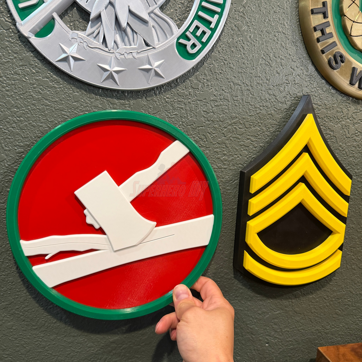 Hand holding the 84th Training Command display insignia plaque on a wall with other military insignias.