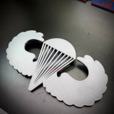 Replica airborne jump wings badge displayed on a black surface, showcasing the iconic wings and parachute design.