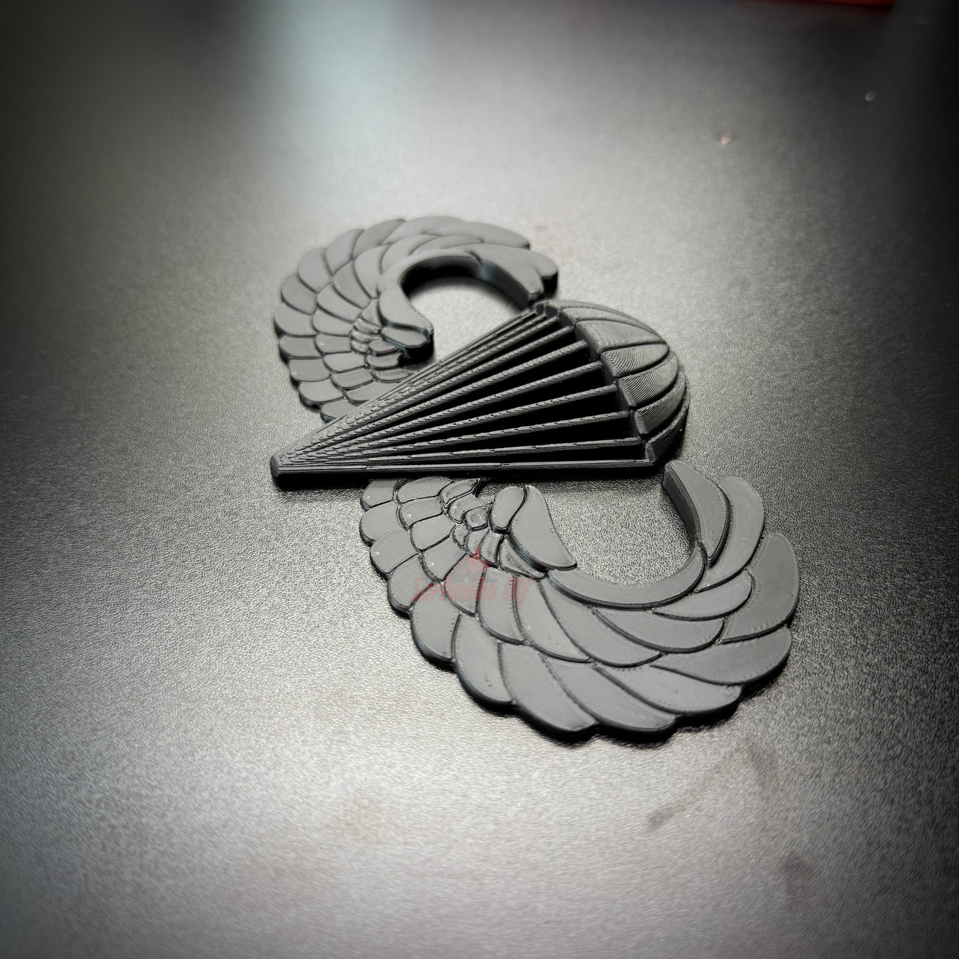 black airborne jump wings badge displayed on a dark surface, symbolizing achievement in military parachuting.