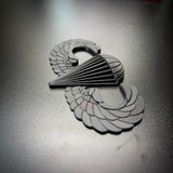 black airborne jump wings badge displayed on a dark surface, symbolizing achievement in military parachuting.